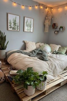 a bed made out of wooden pallets with plants on the bottom and hanging lights above it