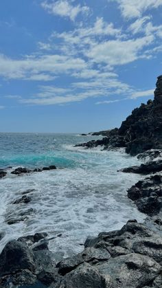 an ocean view with rocks and waves crashing on the shore under a cloudy blue sky