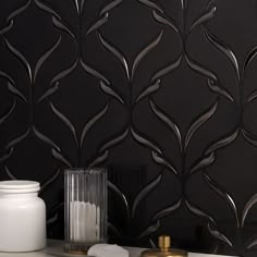 a white vase sitting on top of a counter next to a black wallpaper covered in leaves