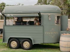 an old fashion food truck is parked in the grass near barrels and other items on display