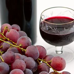 a glass of red wine next to a bunch of grapes