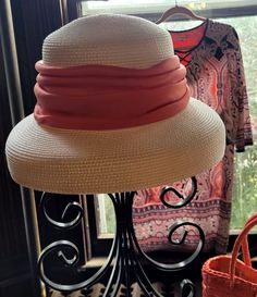 a hat is sitting on top of a stand in front of a window with an orange purse