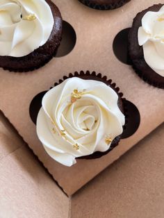 four cupcakes with white frosting and gold decorations in a brown paper box