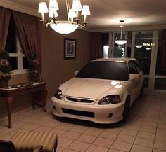 a white car is parked in a room with tile flooring and chandelier