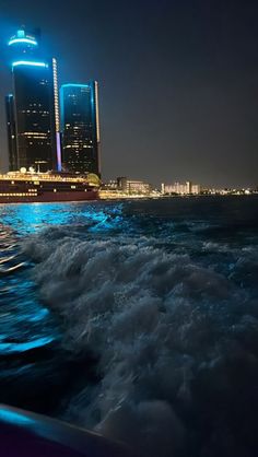 a boat traveling on the water in front of a city at night with buildings lit up behind it