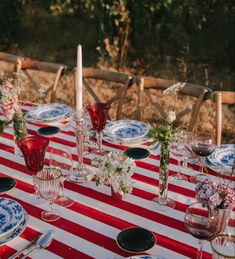 the table is set with plates, glasses and vases for an outdoor dinner party