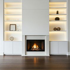 a fire place in the middle of a living room with white walls and shelving