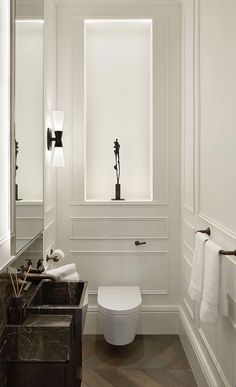 a white toilet sitting next to a bathroom sink under a window in a room with wood floors