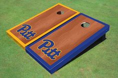 two cornhole game boards with the letters pitt on them, sitting on grass in front of a field