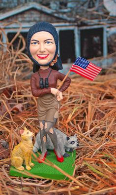 a statue of a woman holding an american flag and two cats on a patch of grass