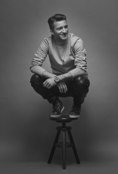 a black and white photo of a man sitting on a stool with his feet crossed