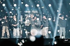 a group of young men standing on top of a stage with lights in the background