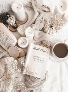 an open book sitting on top of a white blanket next to candles and other items