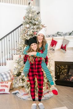 two women are hugging in front of a christmas tree