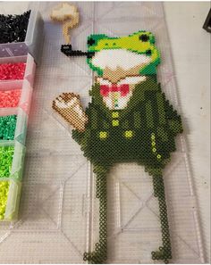 there is a cross - stitch picture of a frog in a suit on the table