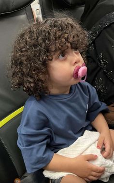 a little boy sitting in a chair with a pacifier in his mouth and wearing a blue shirt