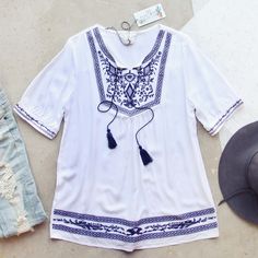 Gorgeous embroidered details adorn this tunic. Designed with a breezy white base, navy embroidered details throughout, a tassel tie neck, short sleeves, and a breezy oversized boho tunic fit. One size fits most. 100% cotton Imported Hand wash cold split One Size Bust 38 Waist 37 Hips 39 Length 30 Bust, waist, and hip measurements are a total circumference. Length is measured from the top of the top to the hem. Measurements are an estimate. Embroidered Tunic For Beach Cover-up In Spring, Embroidered Tunic For Spring Beach Cover-up, Spring Embroidered Tunic For Beach Cover-up, Embroidered Summer Tunic Cover-up, Spring Embroidered V-neck Tunic, Lace Blouses, Oversized Tunic, Boho Tunics, Embroidered Tunic