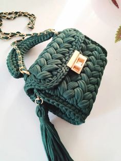 a green handbag with a tasseled handle and chain around it on a white surface