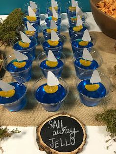 a table topped with cups filled with yellow and blue jello next to a sign