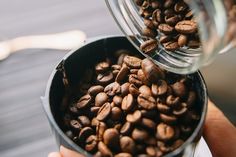 a person holding a container full of coffee beans in their left hand, with the top half open