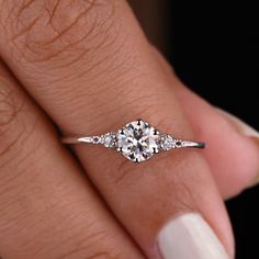 a woman's hand with a diamond ring on top of her finger and white nail polish