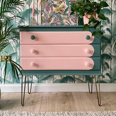 a pink and green dresser next to a potted plant