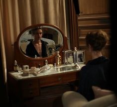 a woman sitting in front of a vanity with a mirror on the wall next to it