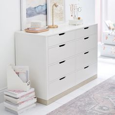 a white dresser sitting next to a wall with pictures on it's top shelf