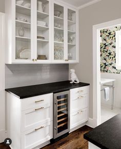 a kitchen with white cabinets and black counter tops, an open wine cooler in the center