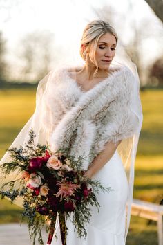 a woman in a wedding dress holding a bouquet and fur stole over her shoulder,