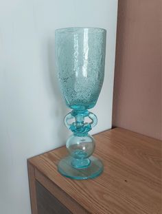 a blue glass sitting on top of a wooden table next to a white painted wall