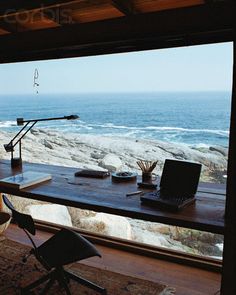 a desk with a laptop on it in front of a window overlooking the beach and ocean