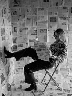 a man sitting in a folding chair reading a paper on top of a wall covered with newspapers