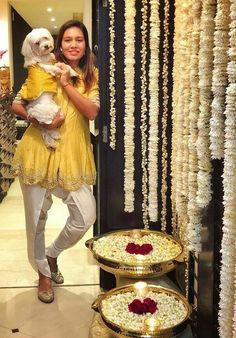 a woman holding a dog in her arms and standing next to two trays filled with flowers