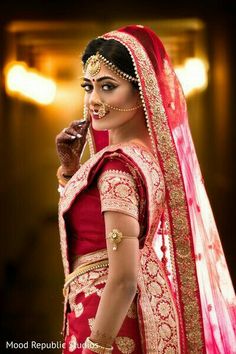 a woman in a red and gold bridal outfit is holding her hand to her ear