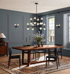 a dining room with blue walls and wooden table surrounded by black chairs, chandelier and rug