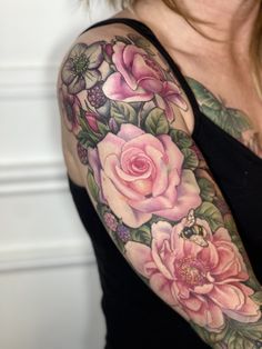 a woman's arm with pink roses and green leaves on her left arm, in front of a white wall