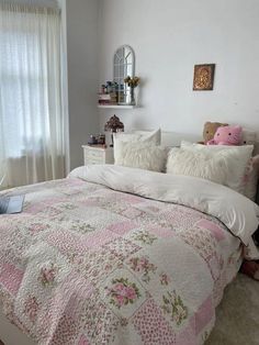 a white bed with pink and green flowers on the comforter in a bedroom next to a window