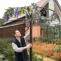 a man standing next to a tree with purple flowers on it