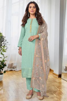 a woman standing in front of a window wearing a green and beige salaf suit