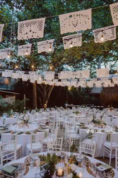 tables and chairs are set up for an outdoor wedding reception with paper lanterns strung from the trees