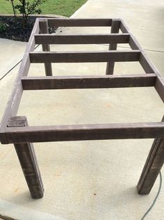 a wooden table sitting on top of a cement ground next to a tree and grass