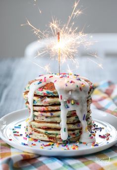 a stack of pancakes covered in sprinkles with a sparkler on top