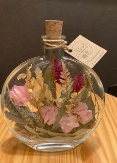 a glass bottle filled with flowers on top of a wooden table next to a tag