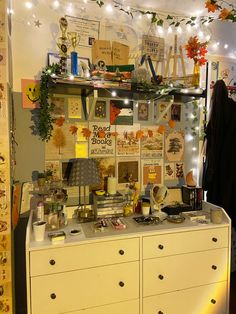 a white dresser topped with lots of clutter next to a wall covered in pictures