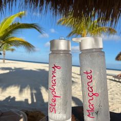 two water bottles sitting next to each other on a beach with palm trees in the background