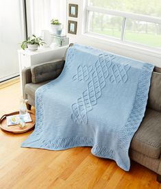 a couch with a blue knitted blanket on top of it next to a window