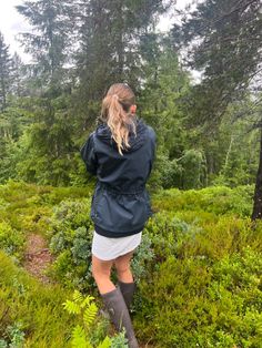 a woman walking through the woods in rain boots and an over - sized blue jacket