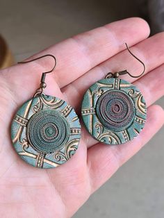 a pair of earrings in the palm of someone's hand, with an intricate design on it