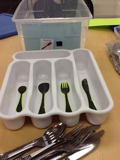 forks, spoons and knives are arranged in an empty plastic container on a table